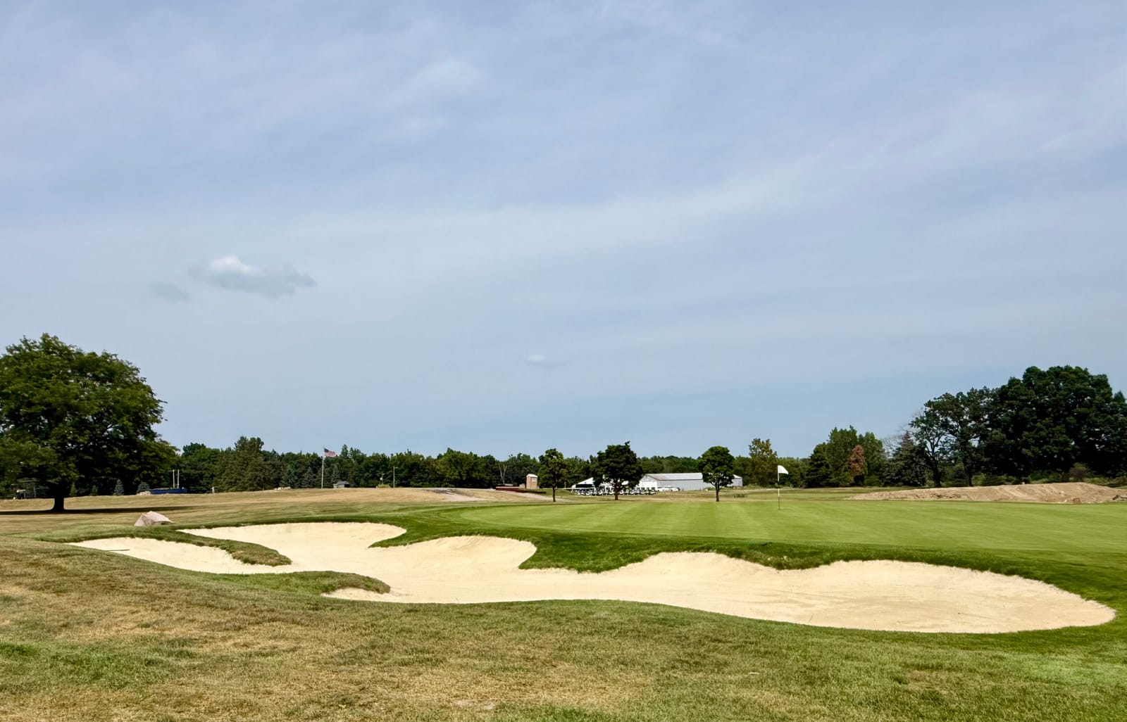 A wide sand bunker complex wrapping the front of a green at Heather Highlands, flagstick in and the cart barn beyond the tree line