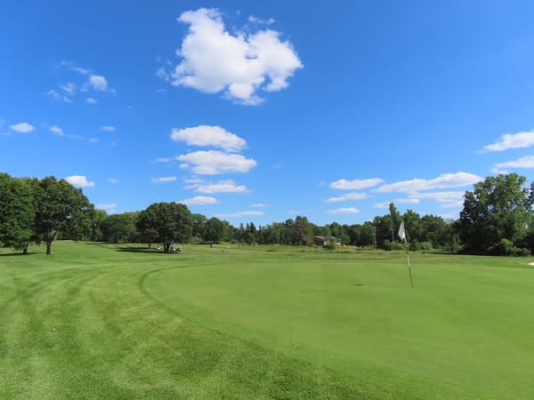 The seventh green under a blue sky, flagstick on the right and the fairway sweeping away to the left
